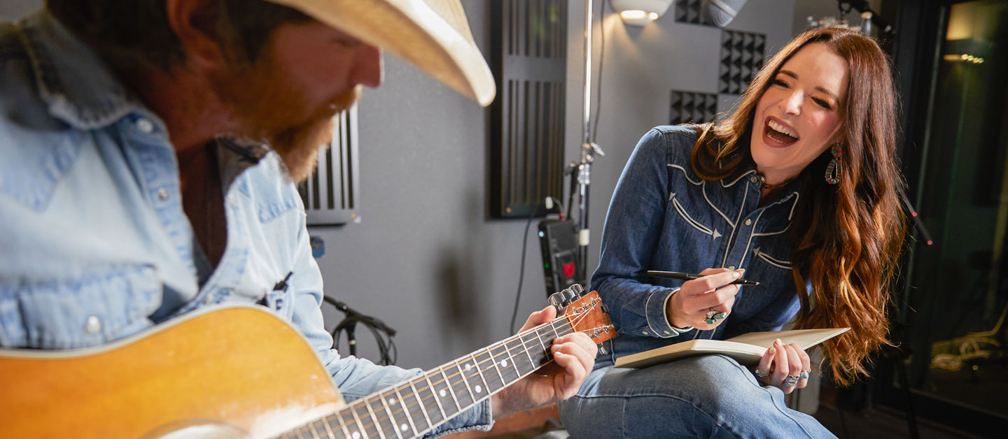 Woman is laughing and looking at her guitar player in studio.